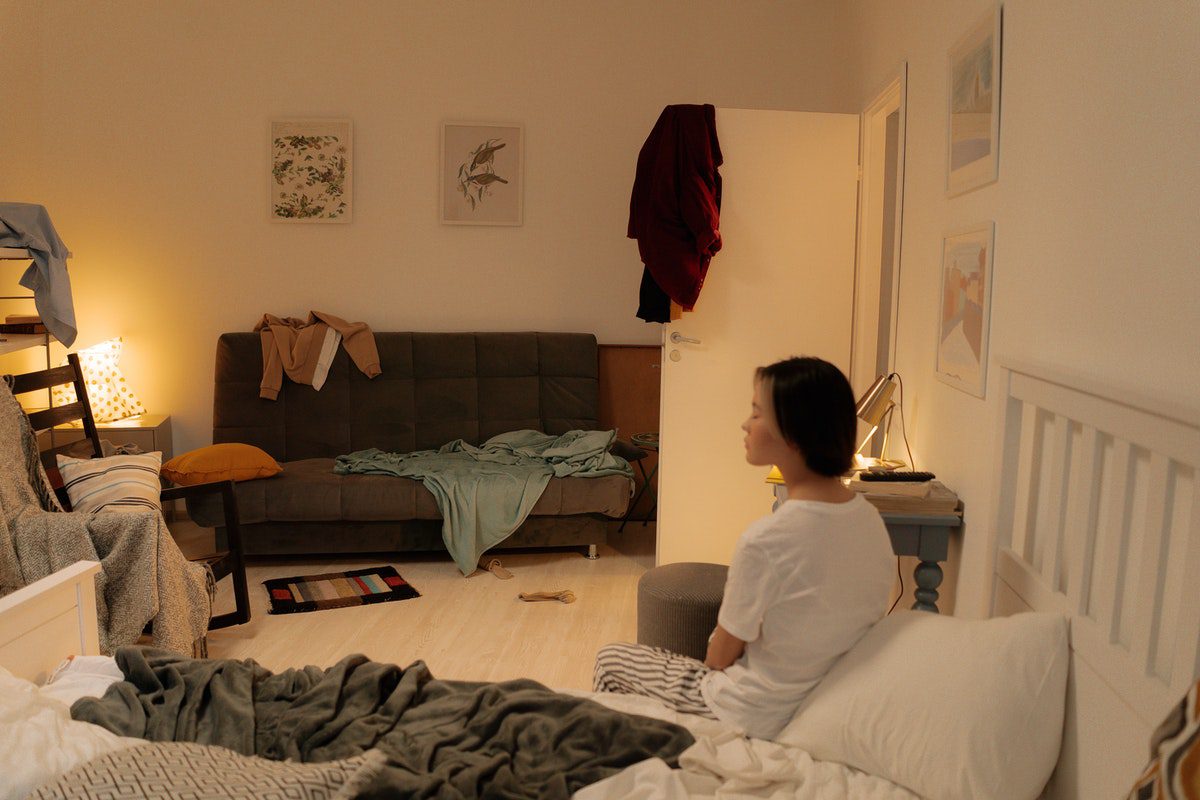 woman sitting in a messy room wondering what to get rid of